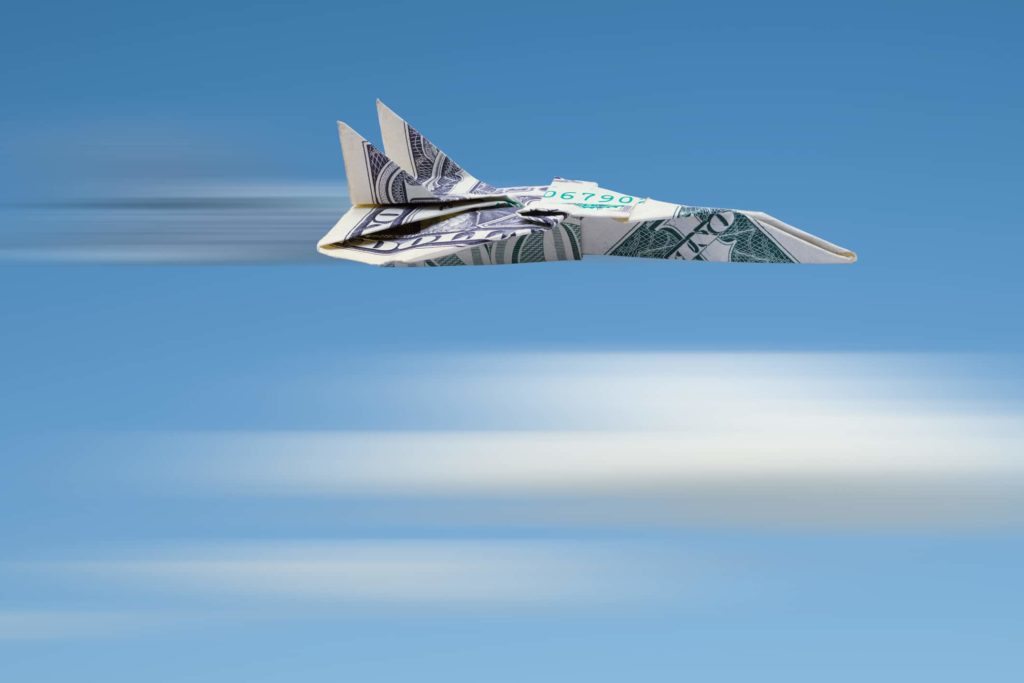 Dollar bill folded up as a paper airplane zooming through the sky.